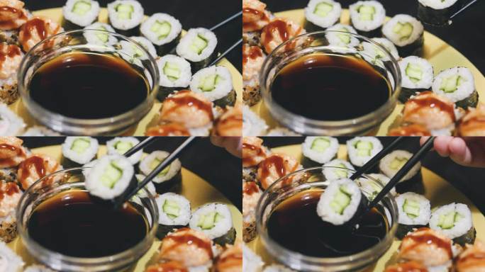 用黑筷子夹起寿司卷，蘸上酱油。