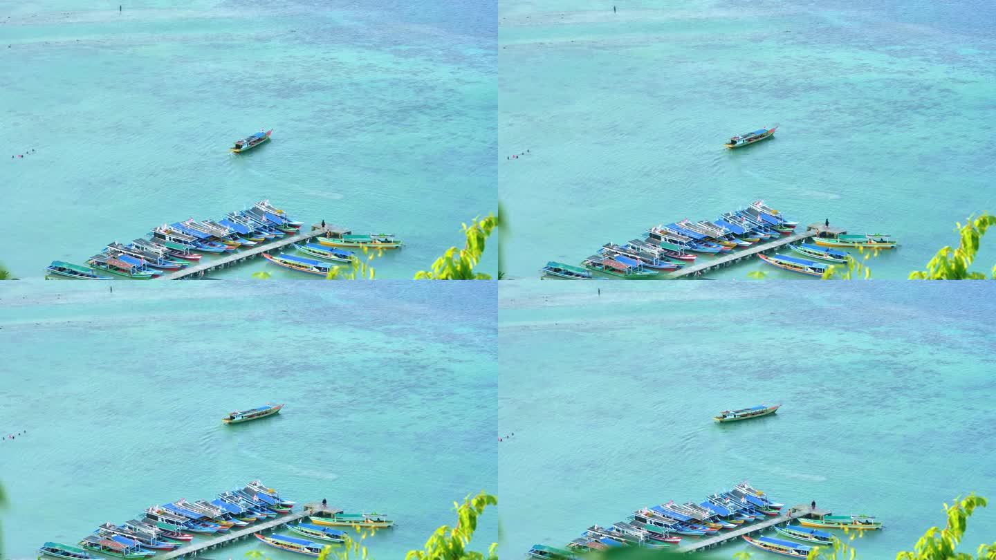 在一个热带小岛的海岸附近，木船穿过平静的蓝绿色水域，小船停泊在那里