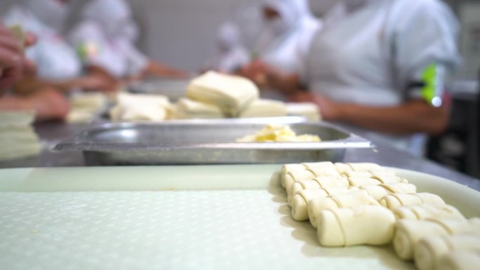 在一家工业面包店里，一群不知名的人把奶酪条卷在酥皮里