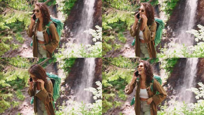 一位兴高采烈的女游客正对着山间的瀑布打电话