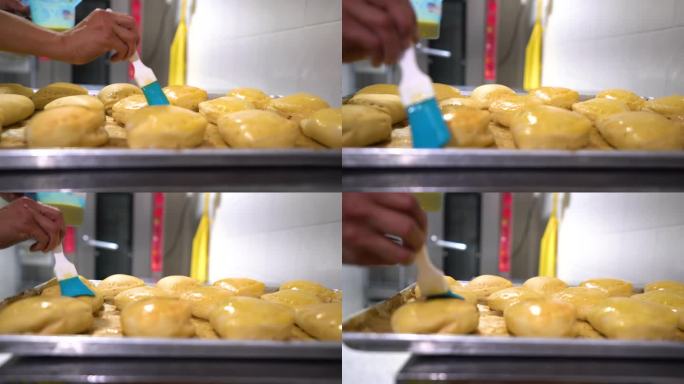 在一家食品加工厂，一名拉丁美洲员工在将肉馅卷饼放入烤箱前用蛋液刷肉馅卷饼
