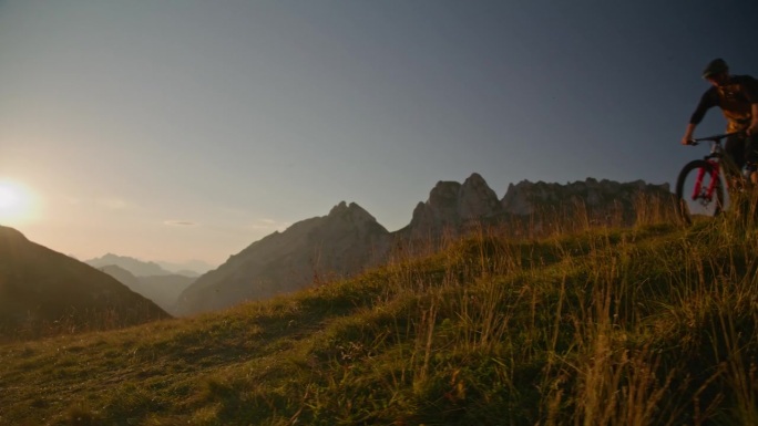 SLO手持拍摄的山地自行车表演特技与自行车在草地上对着晴朗的天空在日落