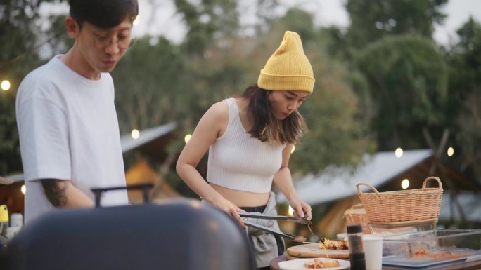 一对年轻的夫妇正在为聚会准备烤肉，并把烤肉放在盘子里