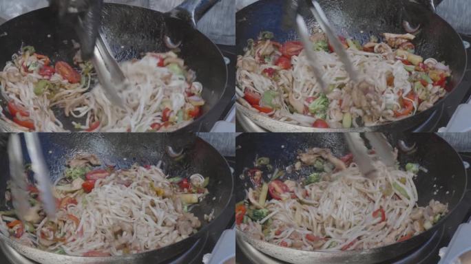 厨师用大钳在炒锅里搅拌面条、肉、蔬菜和调味料。街头食品。特写镜头