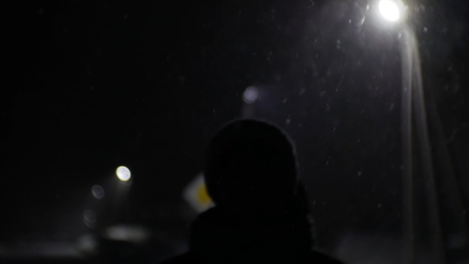 一个女孩的剪影走在雪地上的夜晚。稀有灯柱创造背光。道路标志和花环灯在背景和降雪。电影的情绪。