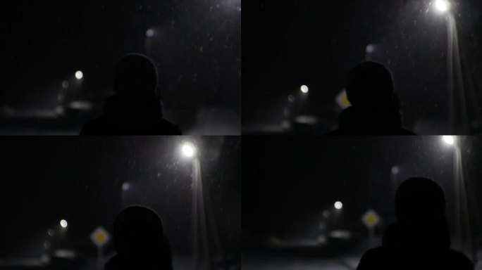 一个女孩的剪影走在雪地上的夜晚。稀有灯柱创造背光。道路标志和花环灯在背景和降雪。电影的情绪。
