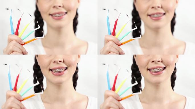 近照:年轻的白种人微笑着，戴着牙托，展示了一套正畸牙刷。白色背景。正畸治疗中牙齿护理的概念