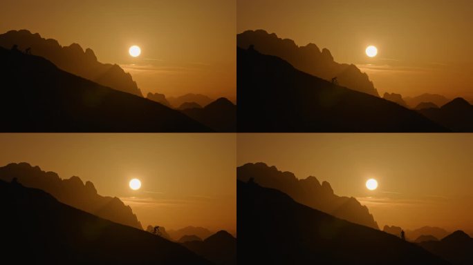 SLO MO低角度远拍的剪影骑自行车在山上对着橙色的天空日落