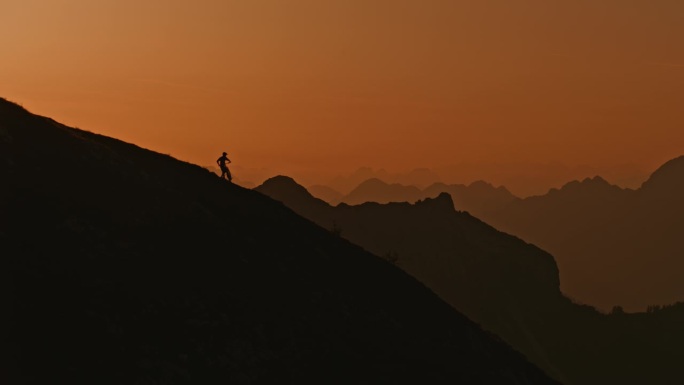 SLO MO低角度锁定镜头的剪影运动员携带和推动山地车上山对抗戏剧性的天空在日落