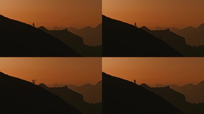 SLO MO低角度锁定镜头的剪影运动员携带和推动山地车上山对抗戏剧性的天空在日落