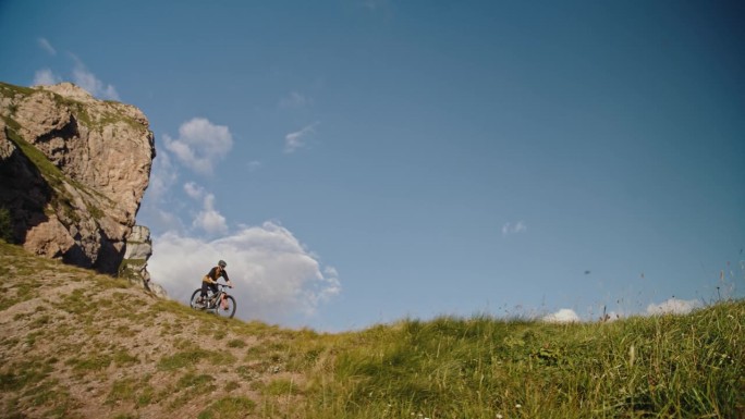 在落基山脉和蓝天的草地上，坚定的骑自行车的男子表演特技的手持镜头