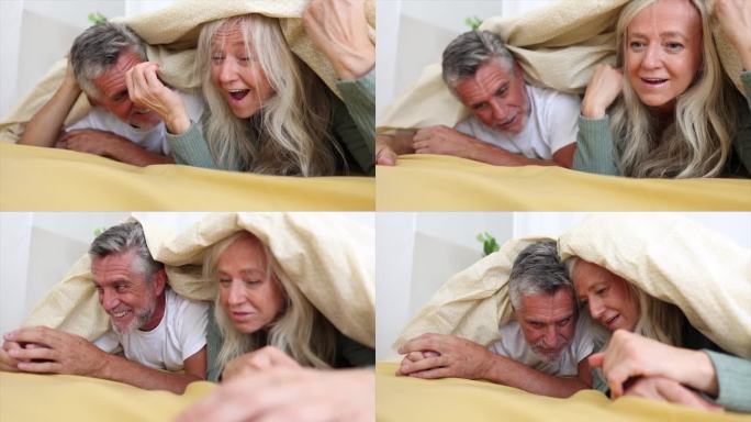 老夫妇盖着毯子躺在床上玩