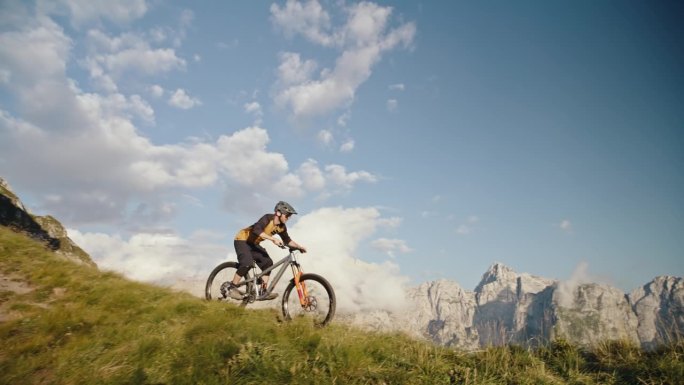 SLO MO手持拍摄的男子骑自行车表演特技，而骑在草地上对落基山脉和蓝天