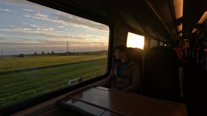 镜头光晕:一位女士坐在窗边，欣赏着晨光中的乡村风光