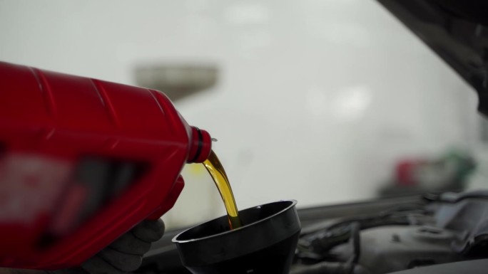 汽车技师在汽车维修厂更换机油，通过漏斗注入新鲜的润滑油。车辆保养，包括更换滤清器，检查油液，优化车辆