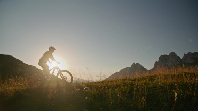 在明亮的夕阳下，坚定的山地自行车手在晴朗的天空下骑自行车的SLO手持镜头