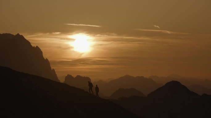 慢动作锁定中距离拍摄的剪影夫妇爬山对戏剧性的天空在日落
