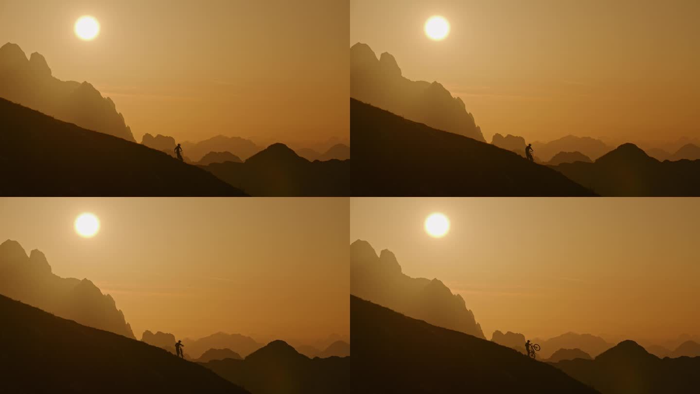 在雾蒙蒙的山脉和壮观的橙色天空下，骑自行车的人的剪影在山上的锁定镜头