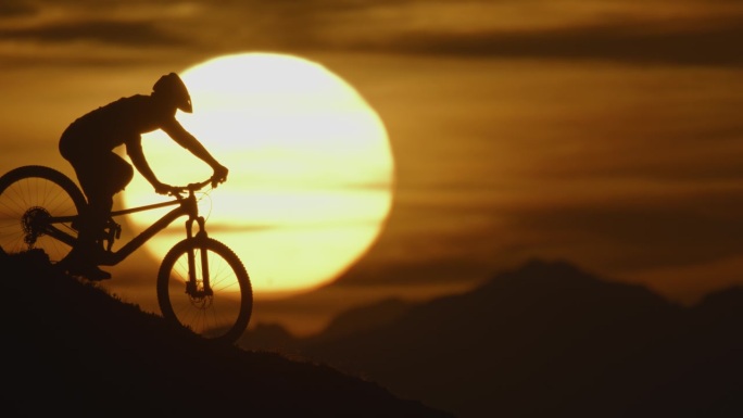 SLO MO锁定拍摄的剪影骑自行车下降和站在山上对雄伟的太阳在日落