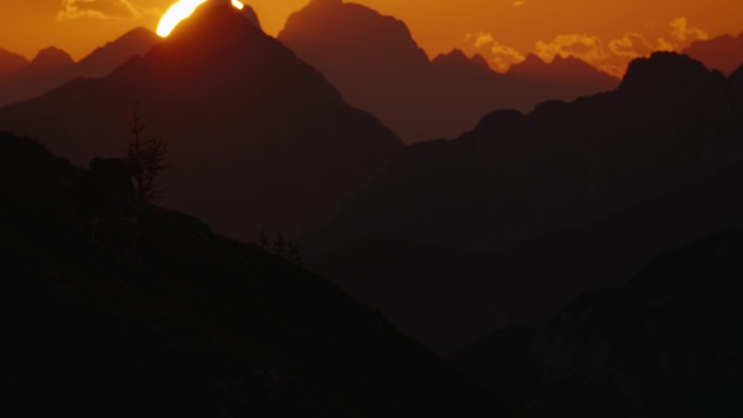 SLO MO手持拍摄的剪影摩托车移动下坡对雄伟的山脉和戏剧性的日落天空