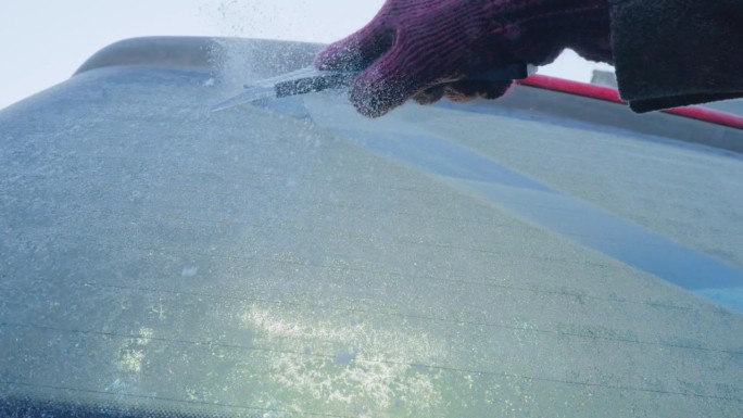 冬天的驾驶——一个女人正在刮掉她汽车后窗上结冰的冰——慢镜头