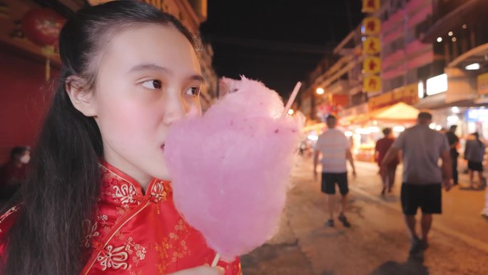 大年初一，一个穿着旗袍的少女在街市上吃棉花糖