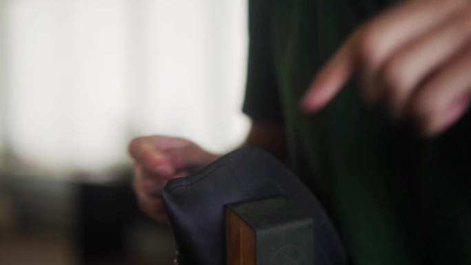 近距离拍摄的专业皮革工匠的手缝制黑色手袋压在保留夹。穿着卡其色t恤的男子在车间制作钱包