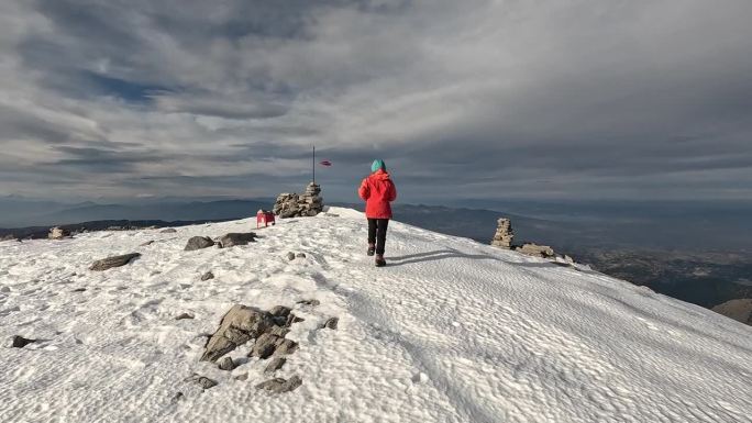 一位女登山者在高海拔雪山的山顶上举起双臂奔跑