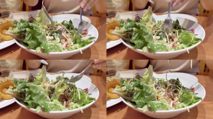 在泰国曼谷的一家餐馆里，一个人用勺子和叉子搅拌一碗蔬菜沙拉的特写。