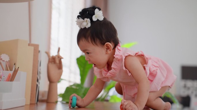 可爱的亚洲女婴，穿着漂亮的粉红色连衣裙，在家里客厅的高桌子上爬，试图够东西。