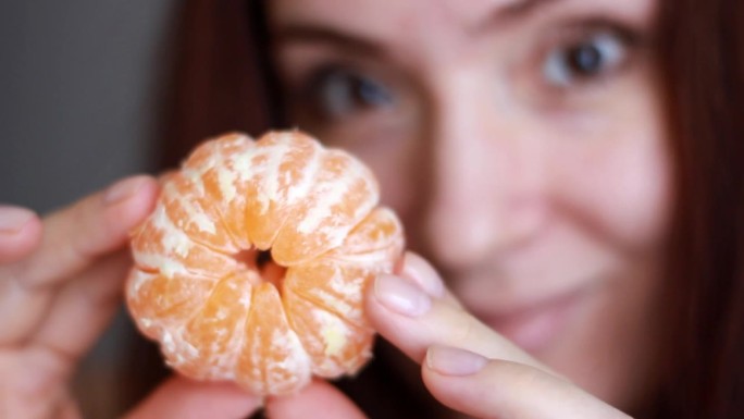特写的女人拿着剥了皮的橘子，享受着香气。一个手里拿着橘子的美女的画像