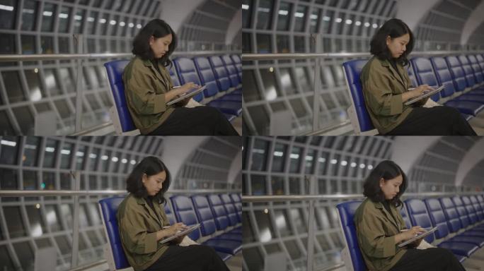 一名亚洲女性坐在机场用数码平板电脑工作。