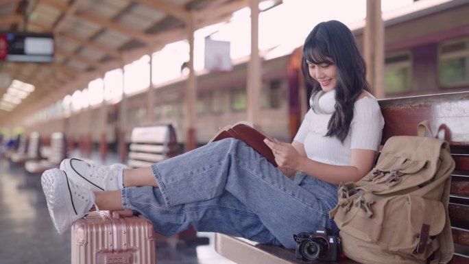 亚洲女游客在火车站等火车，沉浸在小说、旅行和阅读的概念中