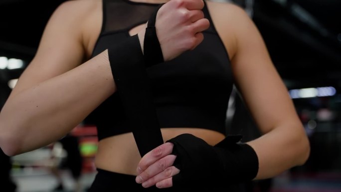 拳头的运动面料。准备泰拳。一位身穿黑色上衣的妇女用黑布包着双手。
