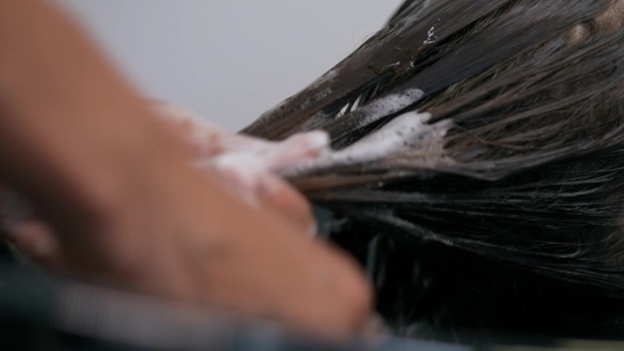 一位女发型师将她的手均匀地涂在躺在椅子上的女孩的湿头发上。特写镜头。