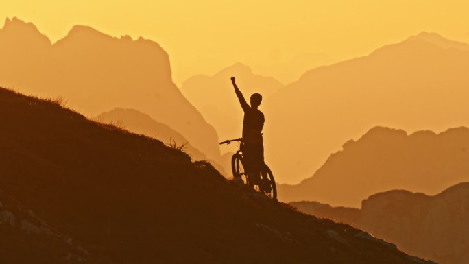 慢动作锁定剪影山地自行车手举起手臂庆祝成功在山上对田园诗般的雾山