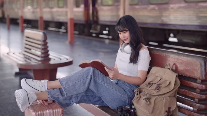 亚洲女游客在火车站等火车，沉浸在小说、旅行和阅读的概念中