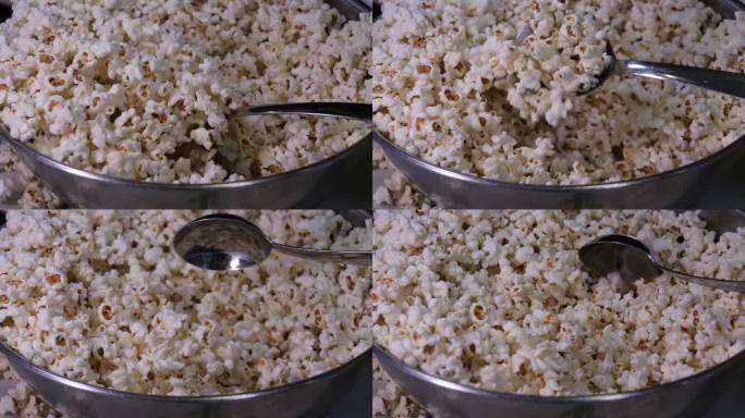用勺子搅拌爆米花(特写)，在铁碗里为晚上看电影准备爆米花