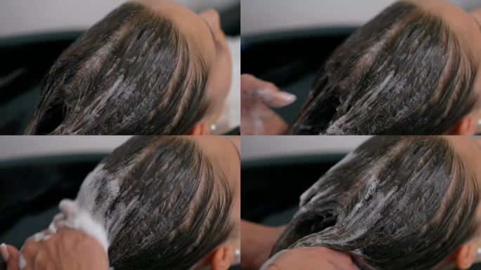 一个女孩的头部特写，湿头发上有洗发水。一位女发型师在她的头发上按摩和分配洗发水。