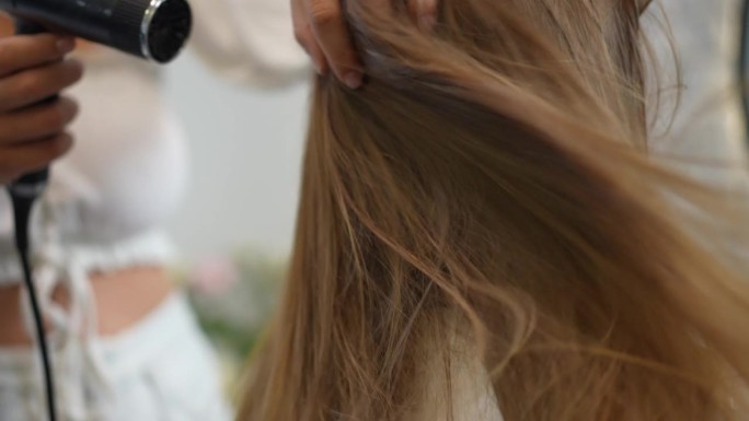 女理发师用吹风机把风吹到女孩的头发上，时不时地用手把头发吹松。特写镜头。