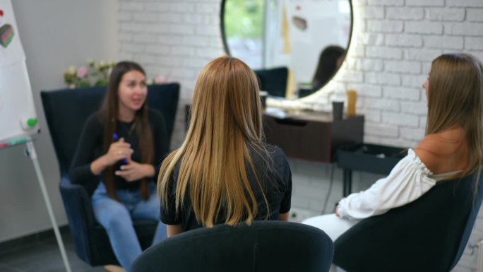 三位女士坐在一家现代美发沙龙的扶手椅上讨论治疗头发和头皮的实用技术。