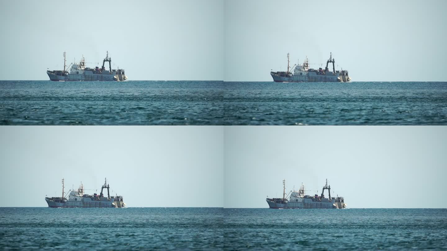 拖网渔船在海上航行时捕鱼。一艘商业渔船在远处的地平线上航行，在平静的海面上捕捉鱼群。商业捕捞海鱼。