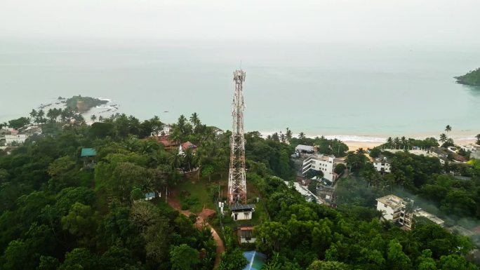 鸟瞰图展示了郁郁葱葱的热带岛屿景观中高耸的通信桅杆，确保了连接，海边小镇可见，这意味着便携性，电信技