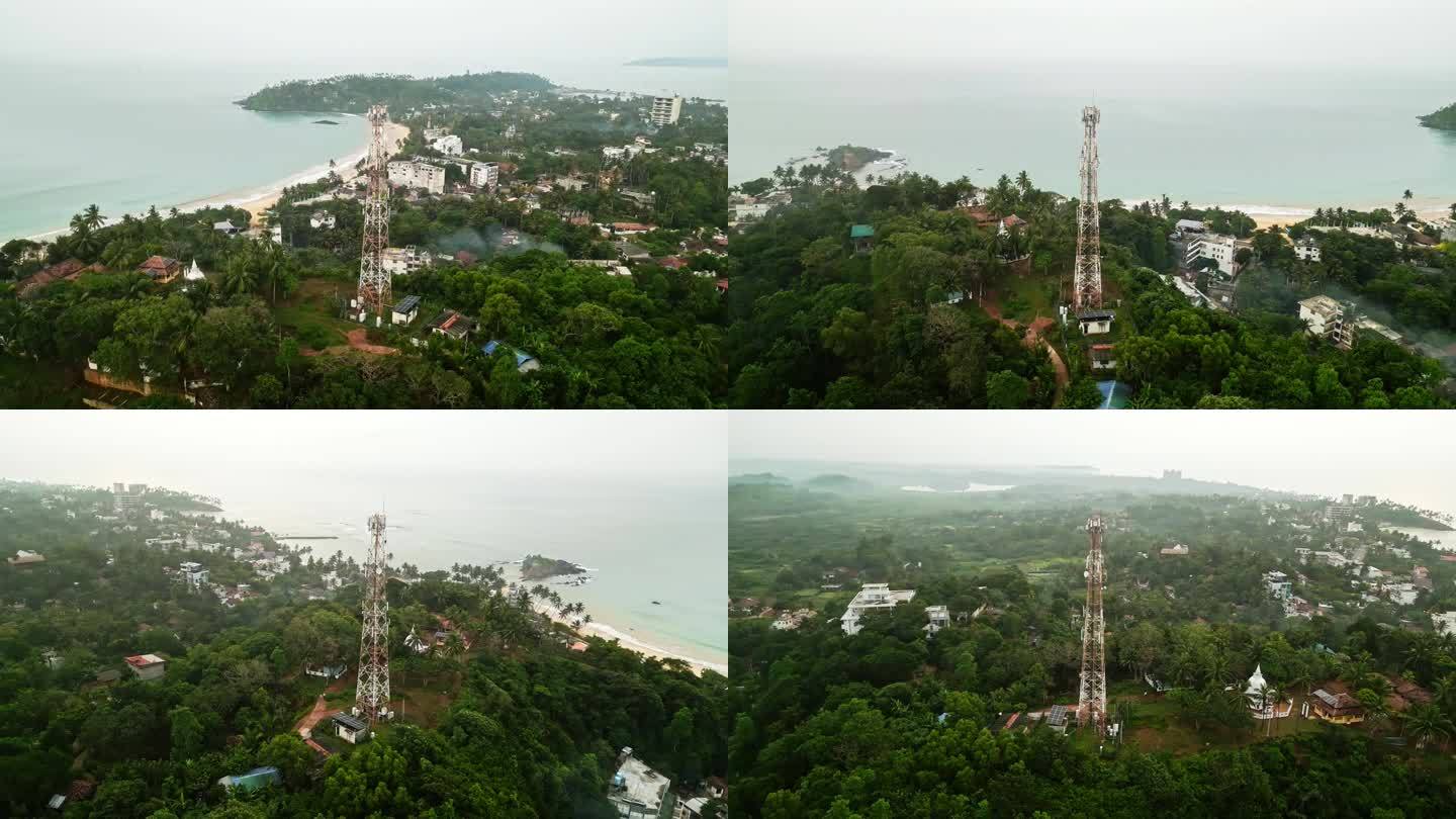 鸟瞰图展示了郁郁葱葱的热带岛屿景观中高耸的通信桅杆，确保了连接，海边小镇可见，这意味着便携性，电信技