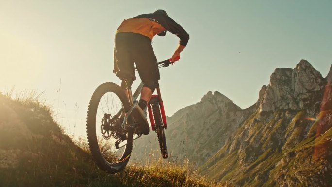 超级慢动作时间扭曲效果男性山地自行车跳跃与自行车越过草坡对田园诗般的落基山脉在阳光明媚的一天
