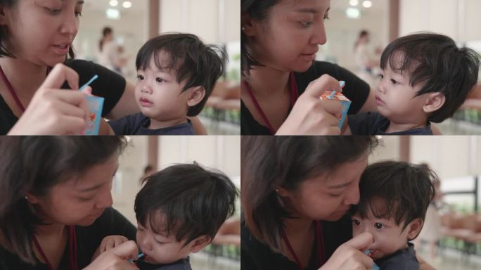 亚洲母亲给男婴喂一盒牛奶。