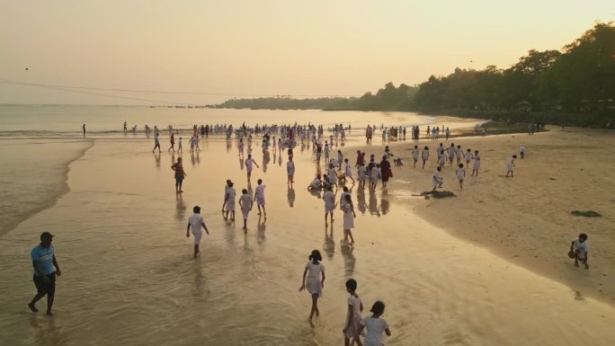 孩子们穿着白色制服在沙滩上欢快地玩耍，海浪拍打着夕阳。群享海边活动体现了无忧无虑的青春，纯真在海边自