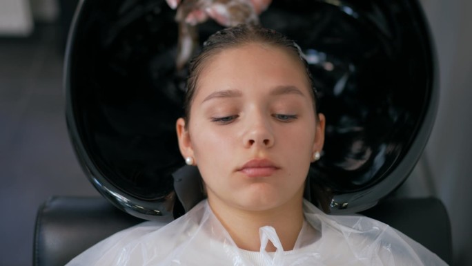 特写镜头。一个女孩躺在美发师的椅子上，湿漉漉的头发上涂着维他命软膏。