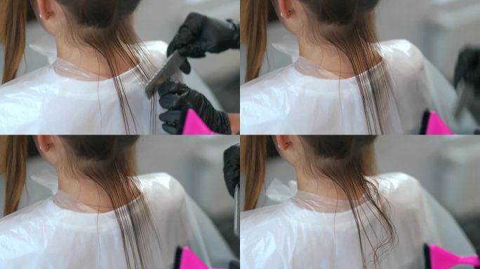一个戴着黑色橡胶手套的理发师正在用梳子梳理一绺头发，一个女孩后脑勺的特写。