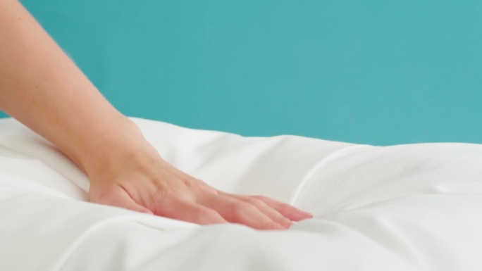 柔软的枕头特写。触摸白色靠垫在蓝色的背景。健康睡眠概念。